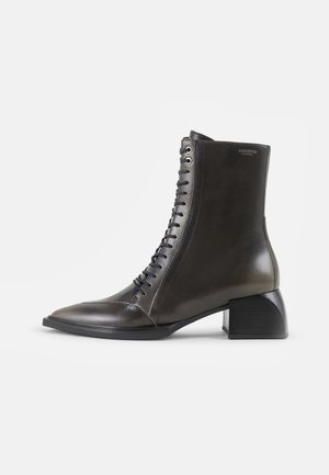 Bottine à lacets en cuir foncé avec un bout pointu et un talon épais. Elle présente des œillets métalliques et une finition lisse et brillante.