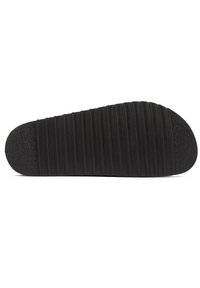 Black rubber shoe sole featuring a textured surface and horizontal grooves, rounded toe, and a distinctive tread pattern for grip.