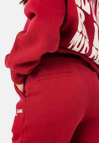 Rode sweatpants en een bijpassend sweatshirt met een gestructureerde afwerking; het sweatshirt heeft gedurfde witte letters. Zakdetails op de broek.