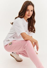 Biela tričko s malými farebnými nášivkami, v kombinácii s ružovými teplákmi s textom "MADE OF SUGAR" a grafikou pandy. Pohodlné tenisky.