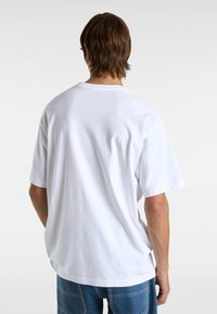 Valkoinen puuvillatee shirt, jossa on löysä istuvuus, pyöreä pääntie ja lyhyet hihat, yhdistettynä sinisiin farkkuihin, joissa on näkyvät ompeleet.