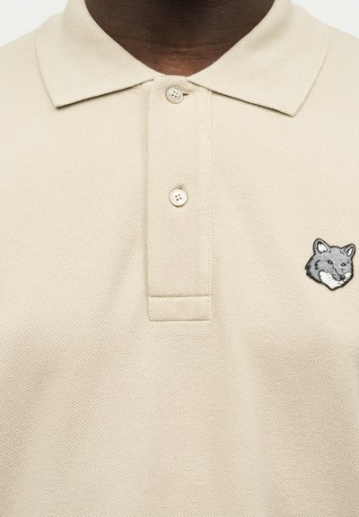 Παντελόνι πόλο σε μπεζ χρώμα με δύο κουμπιά και μικρό γατζωμένο γκρι κεφάλι αλεπούς στο αριστερό στήθος.