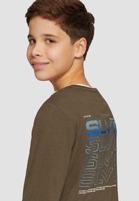 Langsleeve bruin T-shirt met een blauwe grafische print en tekst op de achterkant. Zachte stof, ronde halslijn, comfortabele pasvorm.