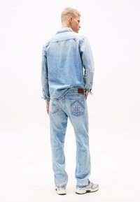 Helles blaues Denim-Hemd und passende Jeans mit einer gemusterten Tasche, lockerer Passform und kontrastierendem braunem Lederbund.