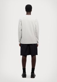 Hellgraues Langarmshirt kombiniert mit dunklen Cargo-Shorts. Besitzt eine lockere Passform, minimale Nähte und gerippte Bündchen. Schwarze Schuhe runden das Outfit ab.
