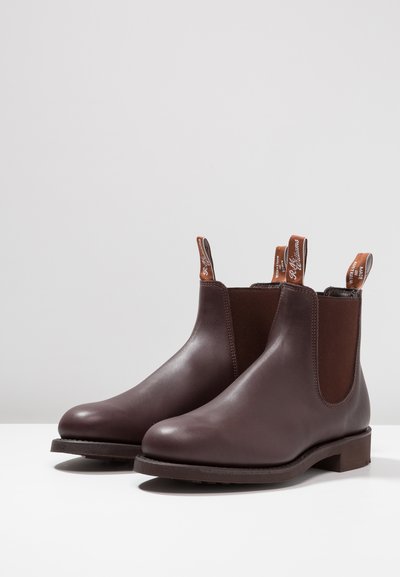 Bottes Chelsea en cuir marron avec des panneaux élastiques latéraux, des bouts ronds et des languettes pour un enfilage facile. Semelles plates robustes améliorant l'adhérence.