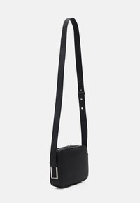 Borsa crossbody in pelle nera con finitura testurizzata, forma rettangolare e un dettaglio in metallo argentato sulla tracolla. Tracolla regolabile in lunghezza.
