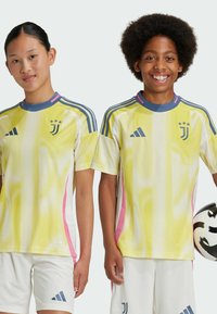 Maglie da calcio giovanile della Juventus in giallo con accenti rosa, realizzate in materiale a rete traspirante, maniche corte e spalle con righe blu.