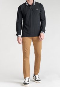 Svart långärmad polotröja med en vitrandig krage, försedd med en logotyp på bröstet. Uppskattad med beige smala byxor och svarta sneakers.