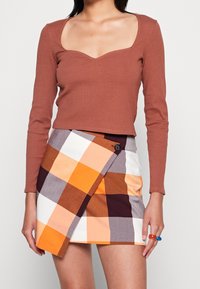 Brun ribbad långärmad topp med fyrkantig halsringning, matchad med en orange, vit och brun rutig omslagsskjorta med knappdetalj.