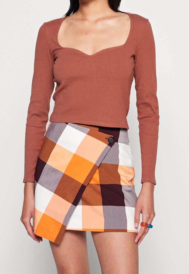 Brun ribbad långärmad topp med fyrkantig halsringning, matchad med en orange, vit och brun rutig omslagsskjorta med knappdetalj.