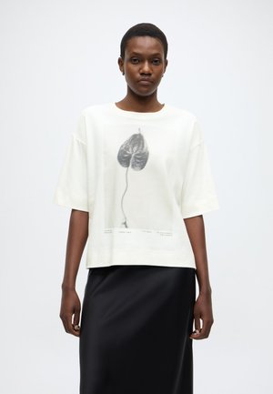 Tricou alb supradimensionat cu imprimeu botanic negru și text, mâneci scurte și croială dreptă, asortat cu o fustă neagră din satin.