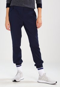 Navy jogger pants with a relaxed fit, featuring side pockets, ribbed cuffs, and worn with white and blue-striped crew socks and light gray sneakers.
