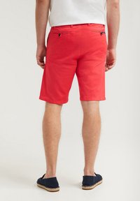 Röda bomullsshorts med rak skärning, synlig sömnad och två bakfickor. Matchas med marinblå espadriller.