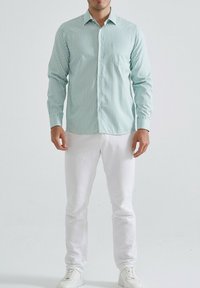 Chemise à rayures vert clair et blanche à manches longues, avec un design à boutons, dotée d'une poche poitrine. Assortie à un pantalon blanc et des baskets blanches.