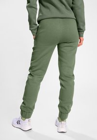 Grüne Jogginghosen mit einem gerafften Bund und Bündchen, aus weichem Stoff. Kombiniert mit weißen Sportschuhen mit grauen Akzenten.