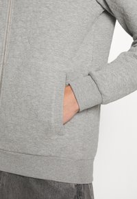 Sweat-shirt gris zippé avec un motif texturé, poignets et ourlet côtelés, doté de poches latérales et d'un tissu lisse et doux.