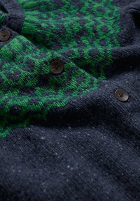 Ciemnoszary sweter dzianinowy z zielonym wzorem, z okrągłymi brązowymi guzikami i teksturowaną powierzchnią, podkreślający intrygujące detale.