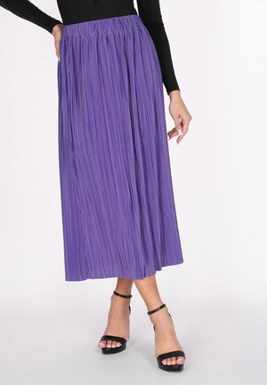 Plissé paarse midi-rok van lichtgewicht stof, met een elastische tailleband en een gladde textuur. Gecombineerd met zwarte sandalen met bandjes.