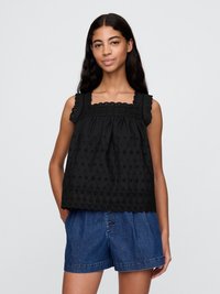 Top nero senza maniche con ricami floreali e orlo scallop, caratterizzato da una scollatura quadrata e tessuto testurizzato. Abbinato a pantaloni di jeans.