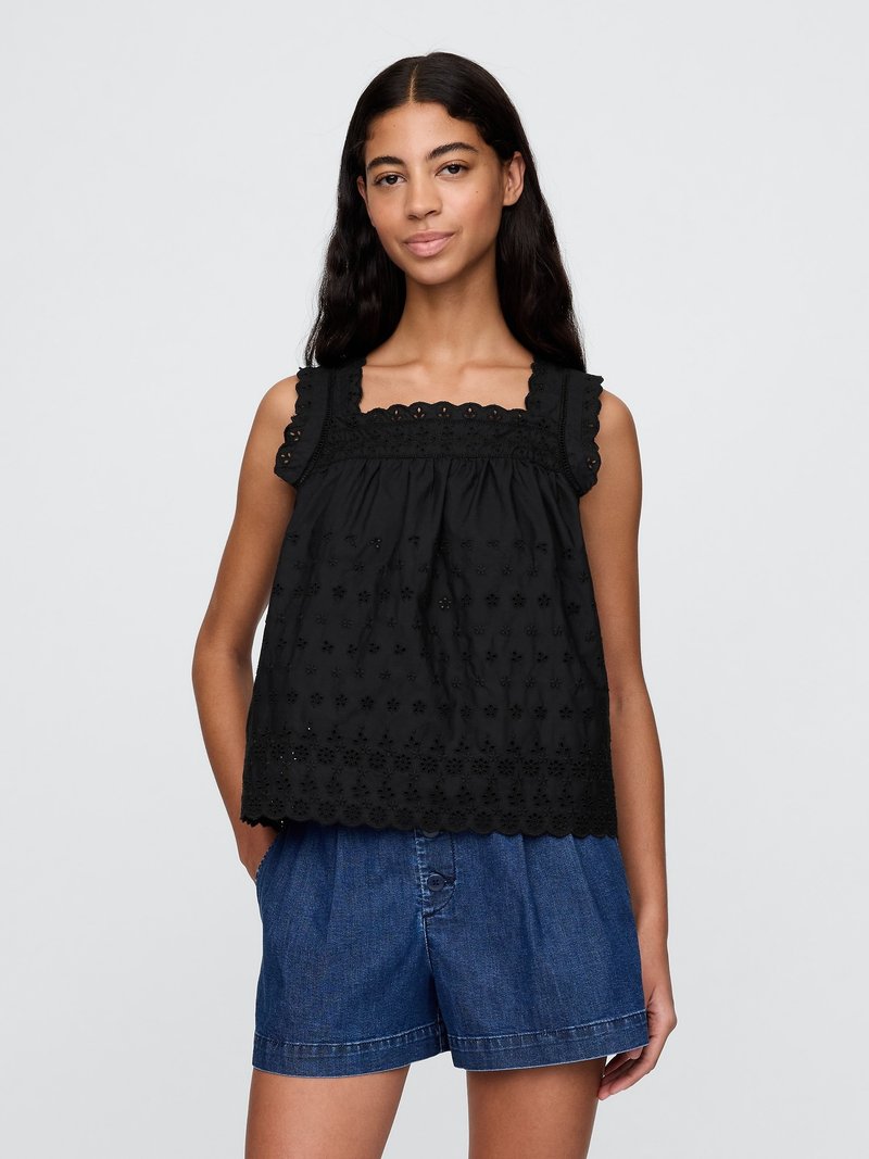 Top nero senza maniche con ricami floreali e orlo scallop, caratterizzato da una scollatura quadrata e tessuto testurizzato. Abbinato a pantaloni di jeans.