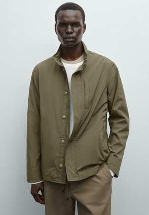 Olive green lightweight jacket with a stand collar, button closure, side pockets, and a smooth texture, worn over a light-colored shirt.