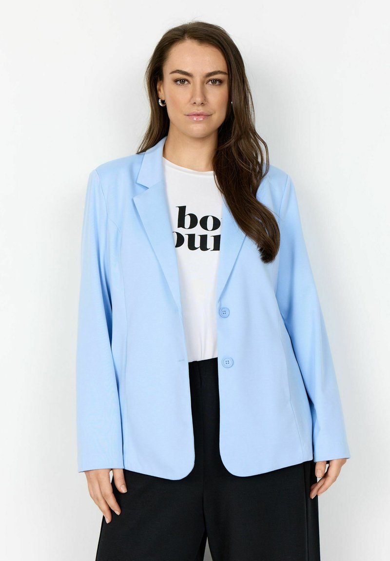 Svijetloplavi sako od glatke tkanine, s reverom s ureznutom prorezom, dva gumba i dugim rukavima, složen preko bijele grafičke majice.