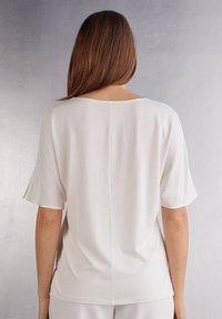 Top de manga corta en color crema, hecho de una tela suave. Presenta un escote amplio y un corte recto, con un sutil detalle de costura central en la parte trasera.