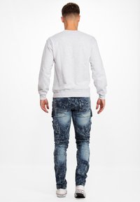 Sweatshirt gris clair à encolure ronde, associé à un jean bleu déchiré avec une coupe slim et des poches de style cargo. Baskets blanches.
