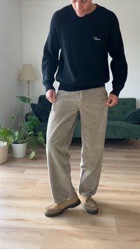 Pantalons en velours côtelé beige à jambes larges, associés à un pull noir à côtes. Les chaussures présentent un design mocassin en beige avec une semelle en caoutchouc.