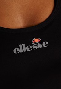 Schwarzes Tanktop aus glattem Stoff mit dem "ellesse"-Logo in Grau und einer kleinen orange-roten kreisförmigen Grafik darüber.