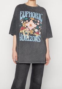 Camiseta de algodón gris de gran tamaño con un diseño gráfico colorido que presenta flores y champiñones, mostrando el texto "HORIZONTES EUPHÓRICOS."