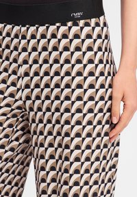 Zwarte en beige gestreepte broek met een herhalend boogontwerp, gemaakt van een gladde stof met een elastische tailleband.