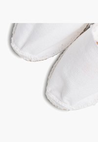 Scarpe slip-on bianche in tela con punta rotonda, superficie texturizzata e dettagli cuciti lungo i bordi.