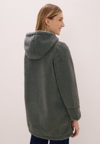 Abrigo con capucha de forro polar en verde oscuro, que presenta una textura suave y un corte relajado, con mangas largas y un dobladillo redondeado.