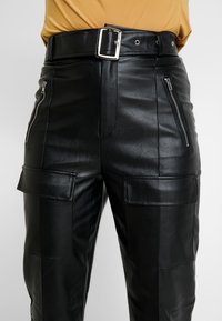 Black leather cargo pants with a smooth texture, featuring silver zip pockets and a wide belt. Includes patch pockets on the thighs.