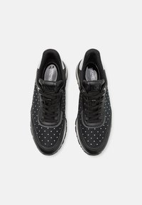 Schwarze Sneakers mit weißen Punkten, ausgestattet mit einer strukturierten Oberfläche, Schnürdesign und kontrastierenden weißen Akzenten an Ferse und Sohle.