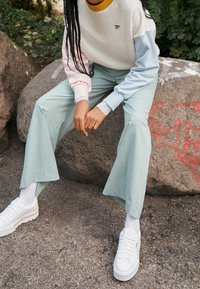 White sweatshirts with pastel sleeves, mint green wide-leg pants, and white sneakers with a beige accent. Natural background with rocks.