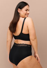 Reggiseno nero con spalline regolabili e chiusura a gancio, abbinato a mutandine a vita alta con un bordo in pizzo sulla cintura.