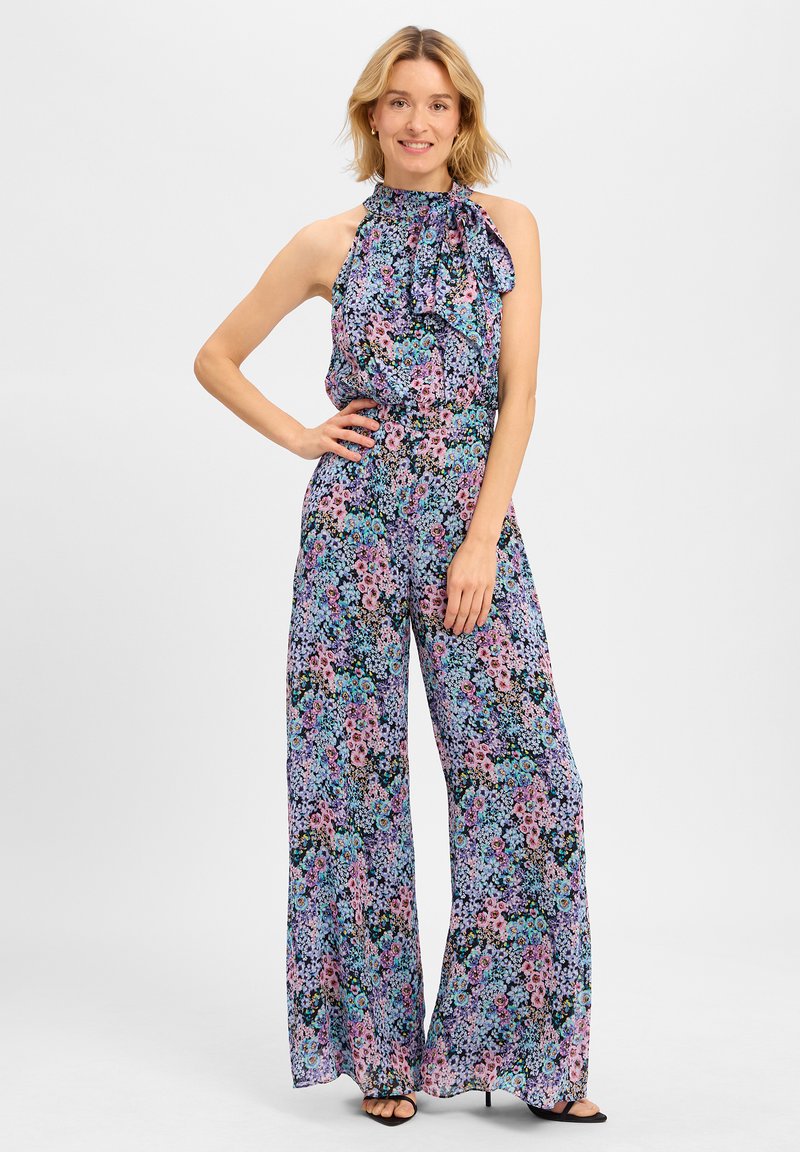 Combinaison florale avec un col halter, des détails volantés, des jambes larges et un motif coloré de fleurs roses et bleues sur fond sombre.