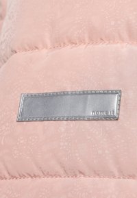 Section d'une veste rembourrée rose avec un motif subtil. Comprend une étiquette rectangulaire en argent avec des bords cousus, affichant le texte "name it."
