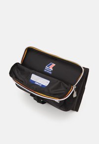 Schwarze Reisetasche mit einem oberen Reißverschluss, gelben und roten Akzenten, einer Fronttasche und einem Logoetikett mit einem leeren Namensschild darin.