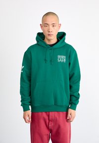 Green cotton hoodie with a front pocket, drawstring hood, and Adidas logo on the sleeve. Features "Sports Club" branding in white.