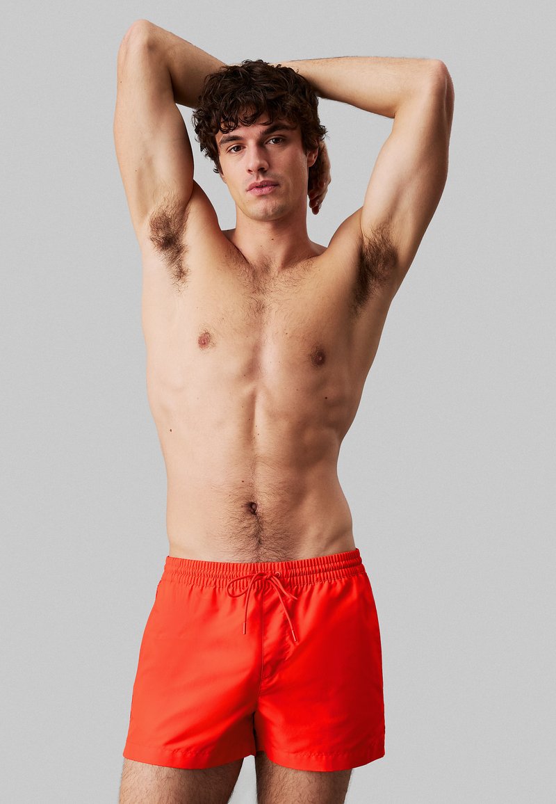 Costume da bagno arancioni con vita elastica e cordoncino. Il tessuto sembra leggero e liscio, arrivando a metà coscia.