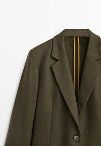 Blazer en mélange de laine vert olive avec un col cranté, une fermeture à un bouton, et un intérieur doublé présentant des rayures jaunes contrastantes.