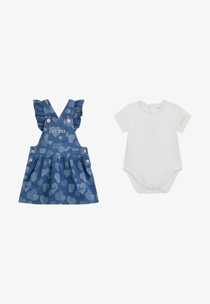 Robe salopette en denim avec des bretelles à volants, motif cœur, et logo "GUESS". Accompagnée d'un body blanc à manches courtes avec un détail de logo.