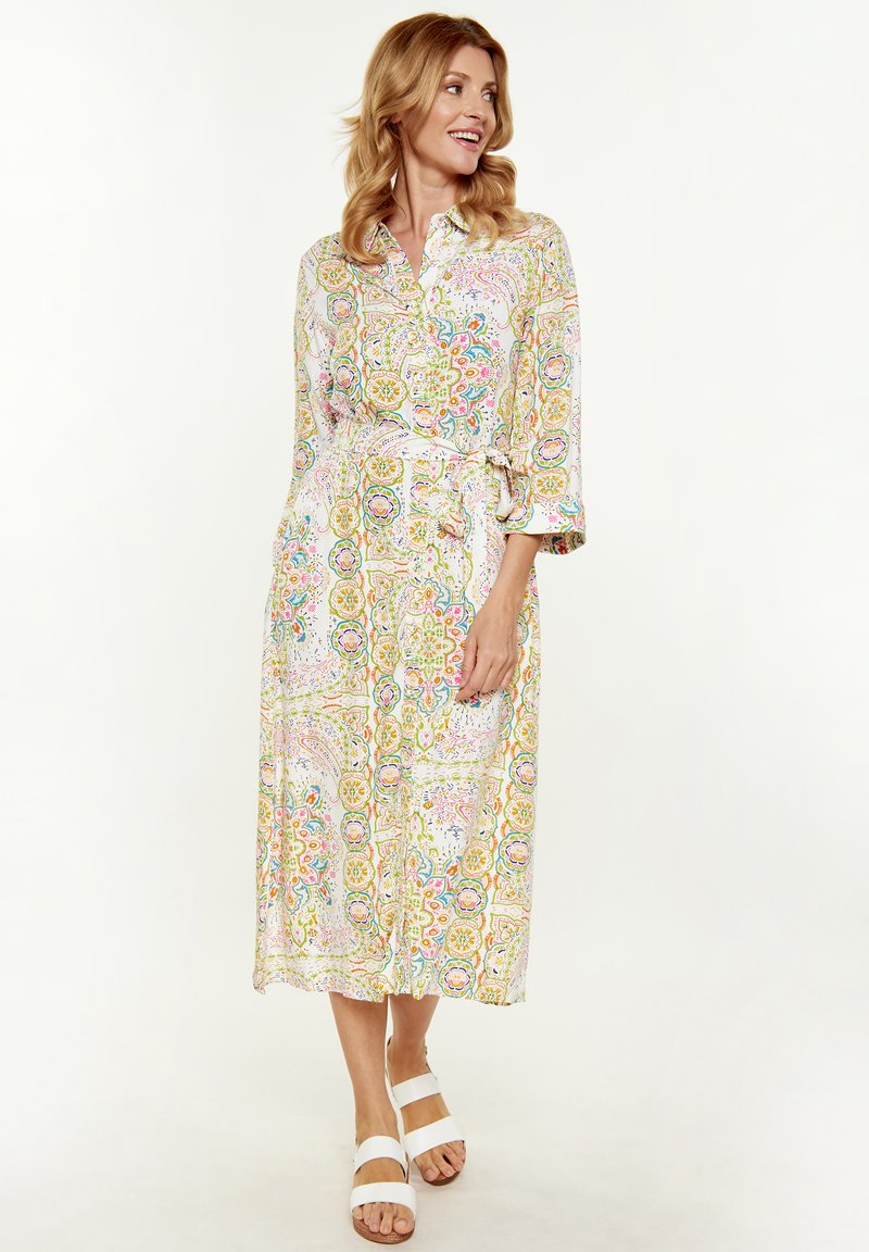 Abito midi con bottoni realizzato in tessuto leggero, con un motivo floreale multicolore, cintura in vita e maniche a tre quarti. Abbinato a sandali bianchi.