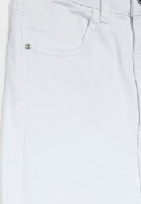 Jean en denim blanc avec une texture lisse, trois poches et des accents en métal argenté sur la poche avant et la taille.