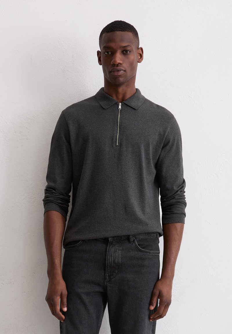 Ciemnoszara, długorękawowa koszulka polo z zamkiem przy kołnierzu. Miękka tekstura, dopasowany krój, noszona z czarnymi dżinsami. Model stoi na jasnym tle.