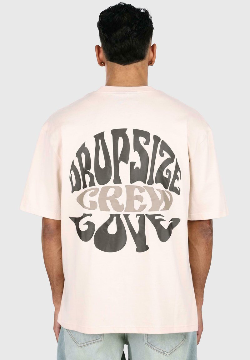 Hellrosa übergroßes T-Shirt aus Baumwolle. Der Rücken zeigt ein grafisches Textdesign in dunkelgrau und beige mit der Aufschrift "DROPSIZE CREW GOVE."